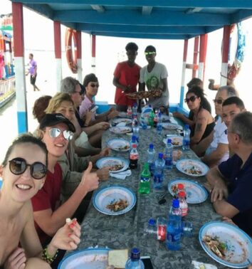 Group of tourists enjoying a seafood lunch together at a long table aboard a shaded boat
