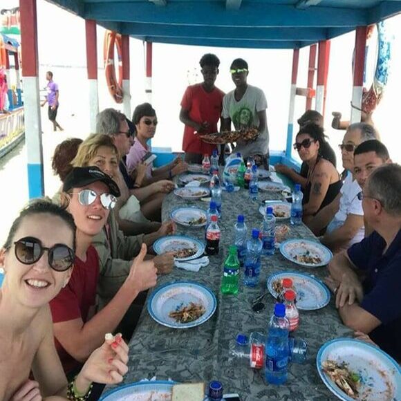 Group of tourists enjoying a seafood lunch together at a long table aboard a shaded boat