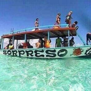 Passengers standing on the upper deck of the excursion boat 'Sorpreso' anchored in clear turquoise water