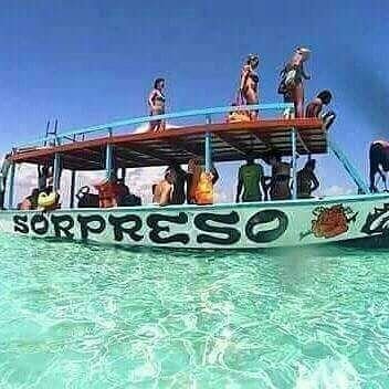 Passengers standing on the upper deck of the excursion boat 'Sorpreso' anchored in clear turquoise water