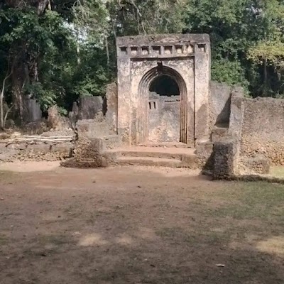 Ancient stone ruins with an arched doorway and carved details, surrounded by forest trees