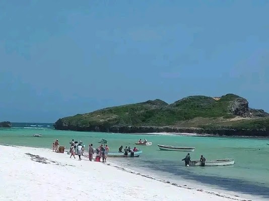 Fishing boats on a white sand beach with turquoise water and a green island in the background