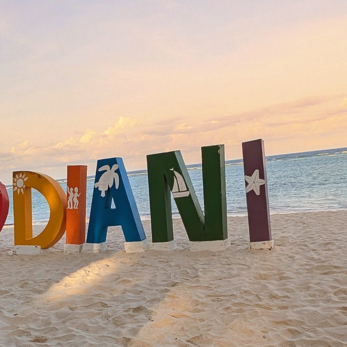 Colorful 'I Love Diani' beach sign with sea-themed icons, standing on the sand at sunset