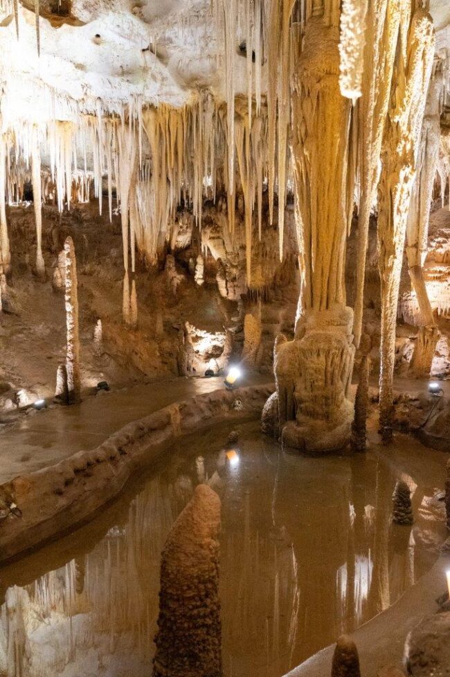 Interior of a limestone cave with stalactites, stalagmites, and a still reflective pool of water