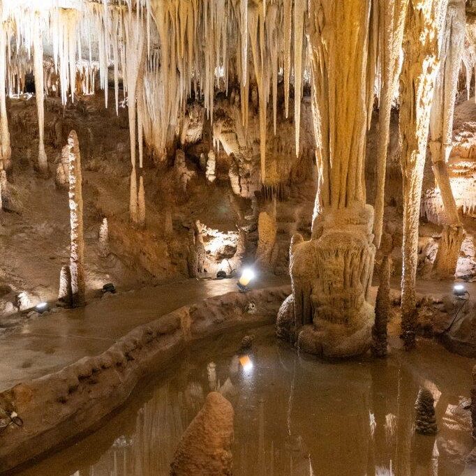 Interior of a limestone cave with stalactites, stalagmites, and a still reflective pool of water